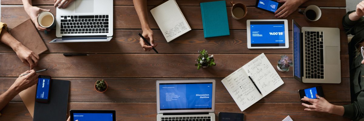 Meetingszene von oben senkrecht auf den Tisch mit Blick auf diverse digitale Endgeräte.