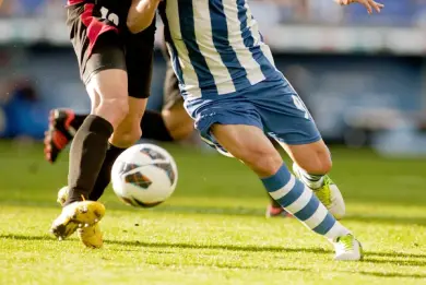 Symbolbild Fussball: Beine zweier Menschen im Lauf mit Fussbll